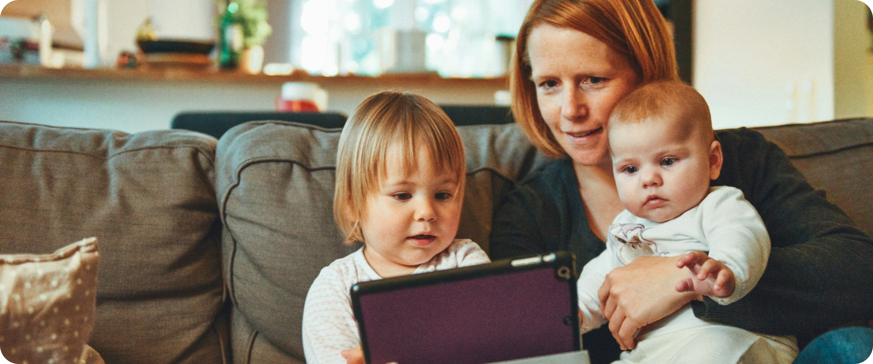 Mother with two children on a sofa - one holding a tablet, the other a baby